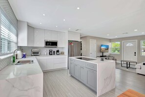 A modern kitchen with white cabinetry, a central island, and a dining area with a sofa.