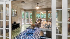 Ein geräumiger Wohnbereich mit Deckenventilator, einer Couch, einem Couchtisch und einem Fernseher auf einem Schrank.