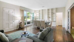 Ein geräumiges Wohnzimmer mit grauem Sofa, einem Esstisch mit Stühlen und einem Bücherregal.
