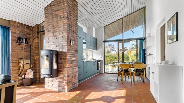 A modern kitchen with a brick fireplace, large windows, and a dining area.