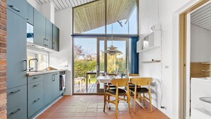 A modern kitchen with grey cabinets, a dining area with wooden chairs, and a view of the garden through large windows.