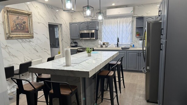 A modern kitchen with a marble island, bar stools, pendant lights, and a microwave.
