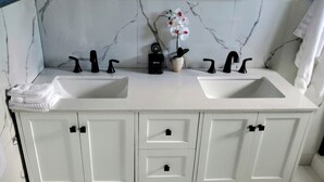 A white bathroom vanity with two sinks, black faucets, and a potted orchid.