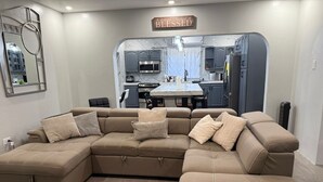 A modern living room with a sectional sofa, a dining area, and a kitchen visible through an archway.