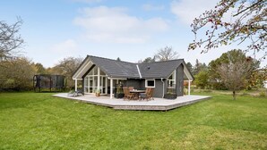 Ein modernes Haus mit einer großen Terrasse, einer überdachten Veranda und einem Trampolin im Garten.