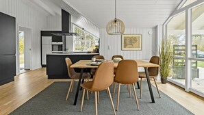 Eine moderne Küche mit einer zentralen Kochinsel, einem Essbereich mit Holztisch und Stühlen sowie großen Fenstern mit Blick ins Freie.