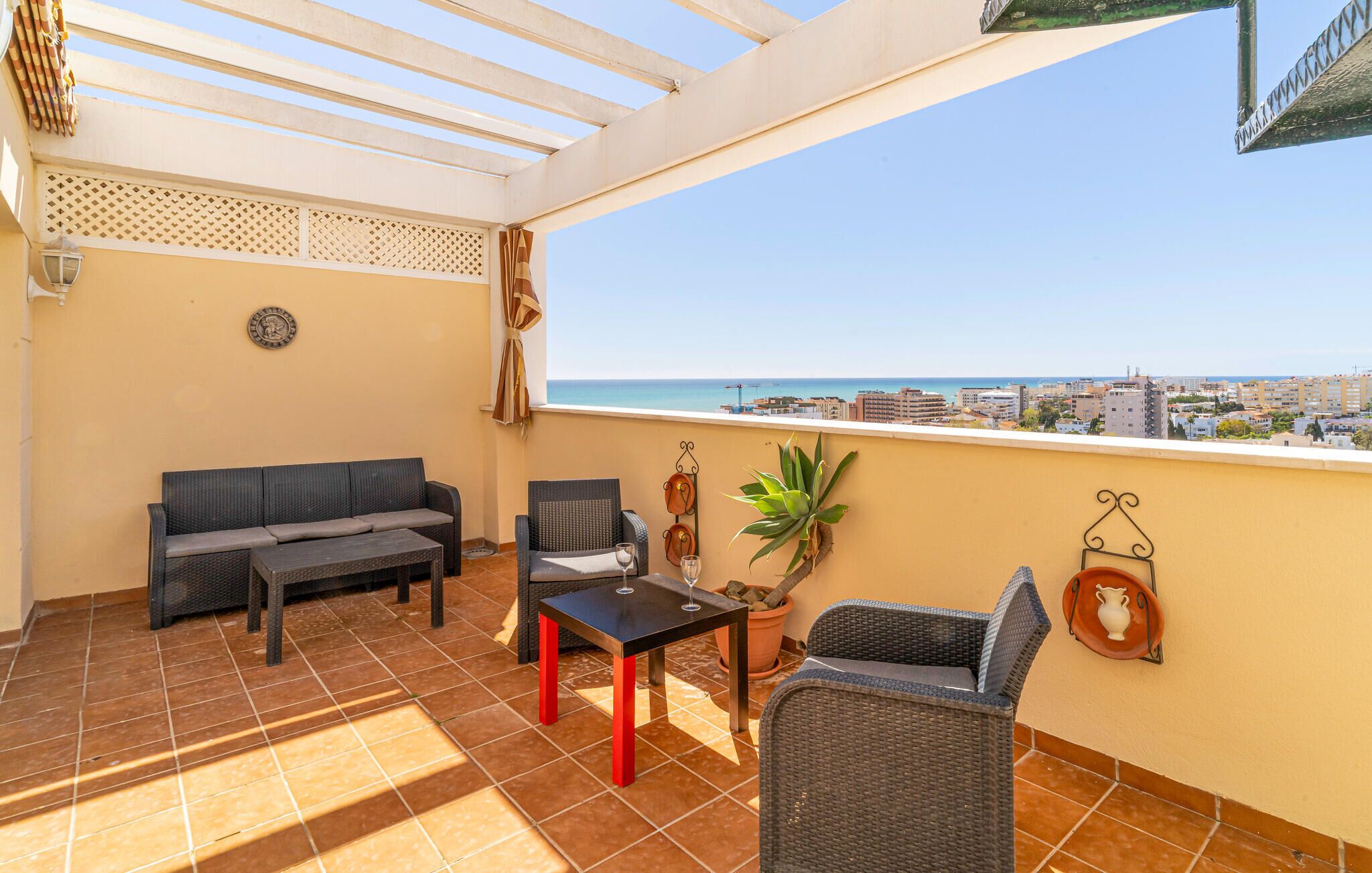 Uma varanda com sofá, cadeiras, mesa e um vaso de planta.