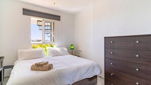 Een slaapkamer met een bed, een dressoir, een raam met uitzicht en een lamp.