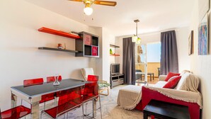 Een moderne woonkamer met een eethoek, een televisie en een bank met rode kussens.