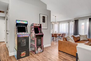 Un salon avec deux bornes d’arcade, un coin repas et un canapé en cuir marron.