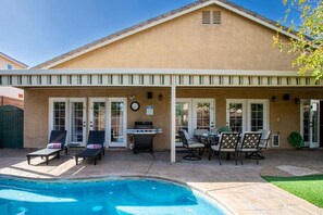 Eine überdachte Terrasse mit Pool, Liegestühlen, Grill und Gartenmöbeln.