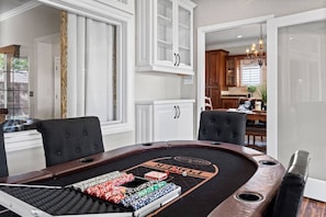 Ein Pokertisch mit Chips und Karten, eine Chandelüster sowie ein Blick in eine Küche und einen Essbereich.