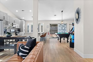 Een moderne keuken met witte kasten, een eetgedeelte met een pooltafel en een woonkamer met een leren bank.