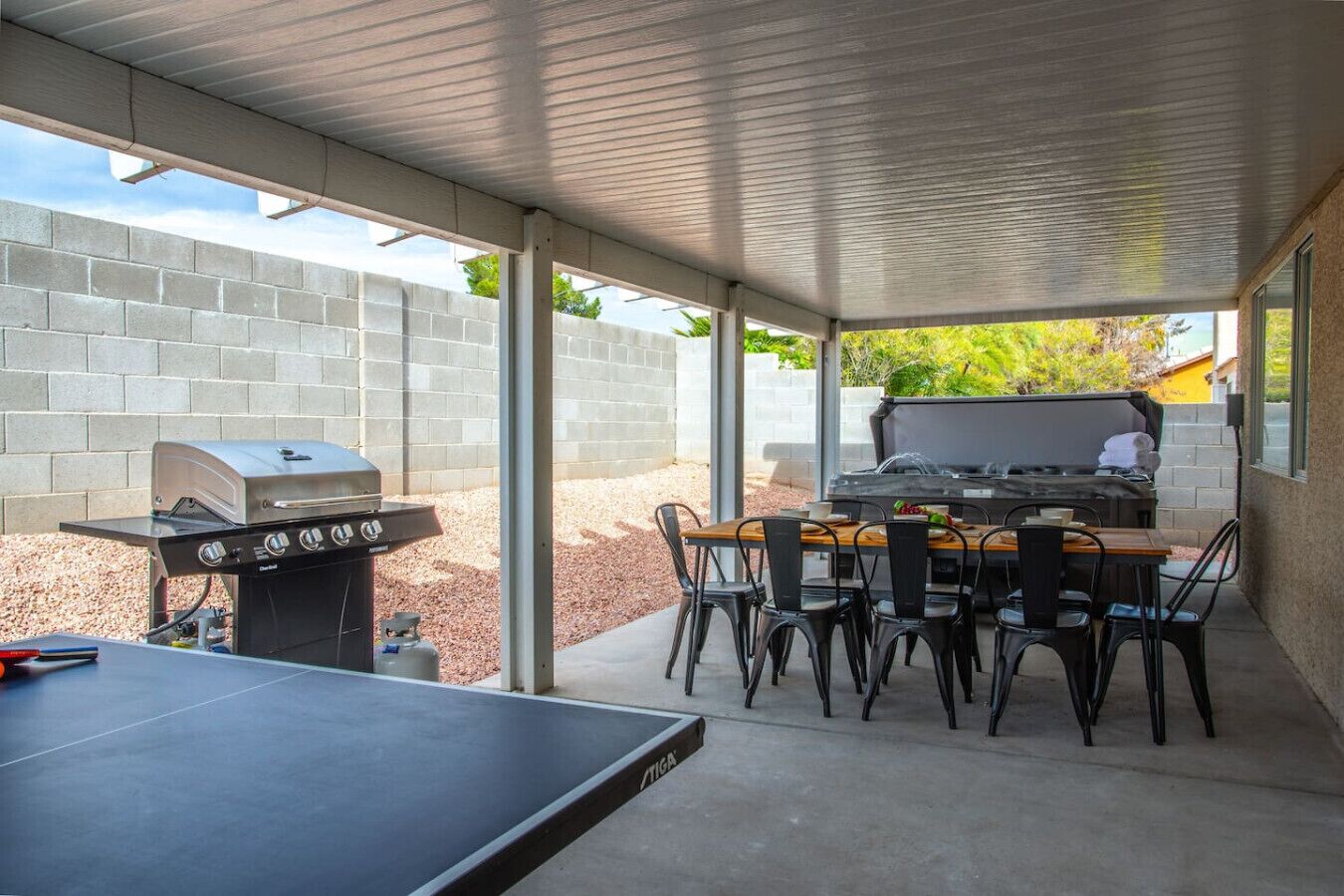 Eine überdachte Terrasse im Freien mit Grill, Tisch und Stühlen.