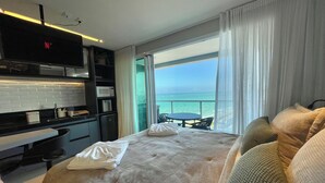 A hotel room with a bed, a small kitchenette, a dining area with a table and chairs, and a balcony with a view of the sea. - RN Studio Premium 916 - Vista Mar (Maceió)