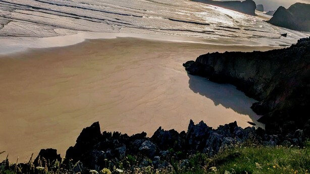 Un paisaje costero con mar tranquilo, costa rocosa y cielo despejado.