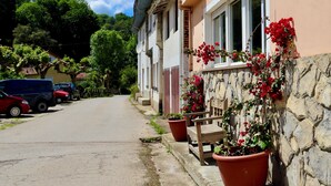 Una calle con coches aparcados, una pared de piedra con plantas en macetas y un edificio con tejado de baldosas.
