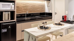 A modern kitchen with built-in appliances, a dining area with a marble table, and a flat-screen TV mounted on the wall. - RN Studio Premium 917 - Vista Mar (Maceió)