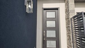 Un edificio moderno con una parete esterna blu scuro, una porta grigia con un pannello di vetro e un piccolo fiorile a parete.