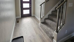 Un corridoio con pavimento in legno, una porta con finestra e una scala con ringhiera in metallo.