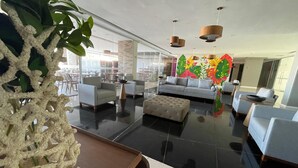 A modern hotel lobby with a sofa, armchairs, a coffee table, and a decorative plant. - RN Studio Premium 918 - Vista Mar  (Maceió)