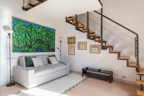 Una sala de estar moderna con un sofá, una mesa de centro, un cuadro, certificados enmarcados y una escalera singular.