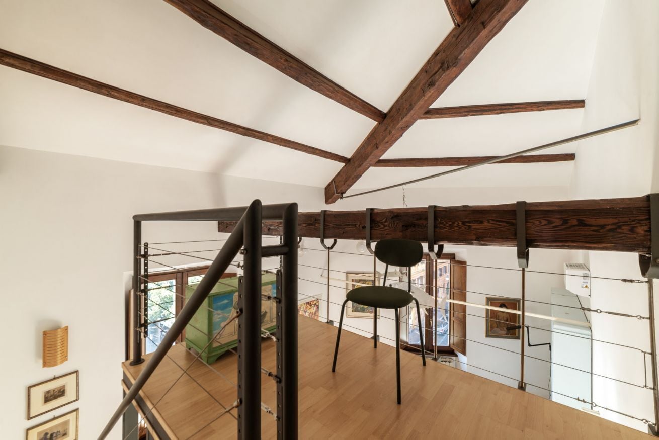 Eine Holztreppe mit Metallgeländer, ein grüner Stuhl und Blick auf einen Raum mit Gemälde und Fenster.