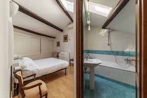 Une chambre à coucher comprenant un lit, une table de chevet et une chaise. À côté se trouve une salle de bain avec un lavabo, une baignoire et une douche.