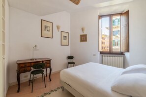A bedroom with a bed, a desk, and a chair. There are framed pictures on the wall and a window with a view of buildings. - Manara 29 - FromHometoRome (Roma)