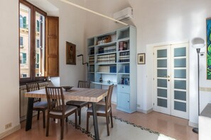 A dining area with a wooden table and chairs, a bookshelf, and a white door with frosted glass panels. - Manara 29 - FromHometoRome (Roma)