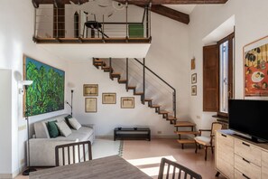 A spacious living room with a high ceiling, a staircase, a sofa, a dining table, and a television. - Manara 29 - FromHometoRome (Roma)