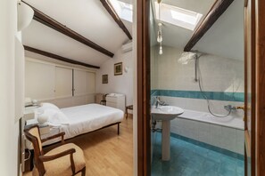 A bedroom with a bed, bedside table, and chair. Adjacent is a bathroom with a sink, bathtub, and shower. - Manara 29 - FromHometoRome (Roma)