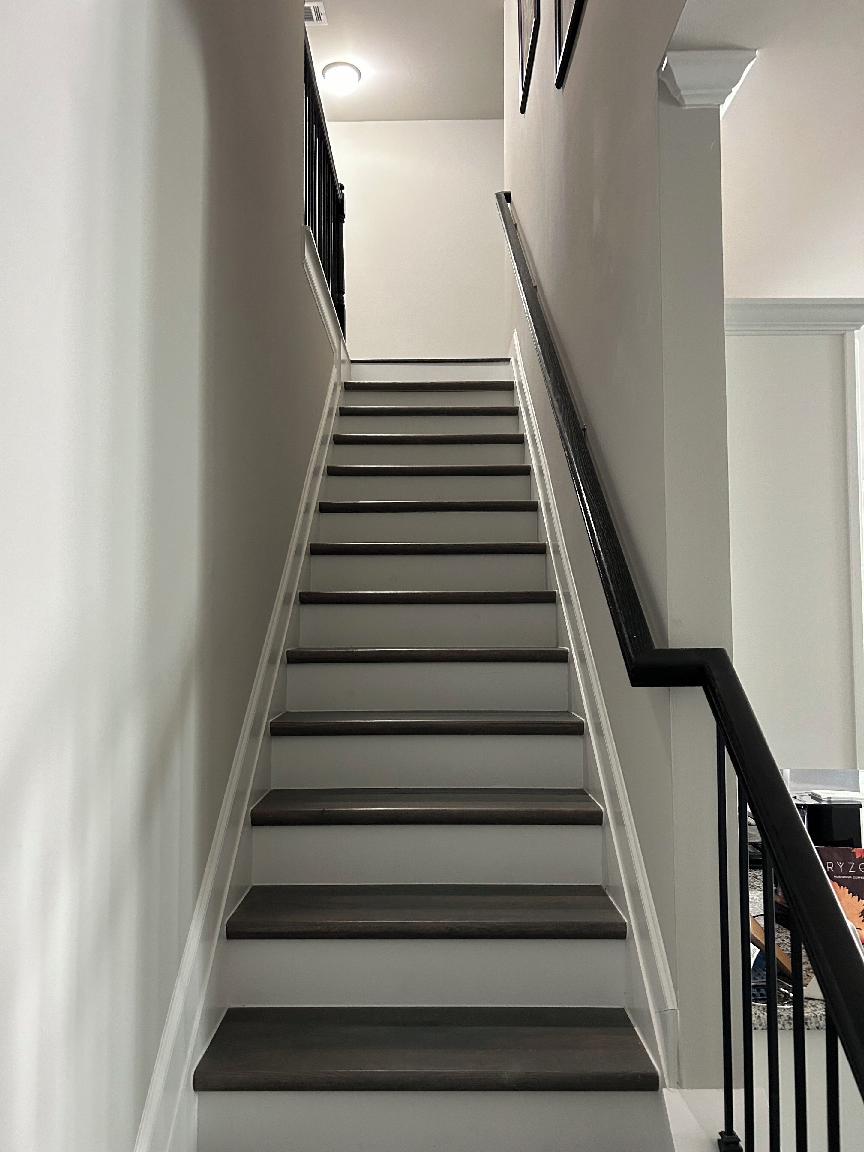 A staircase with dark wooden steps and white walls, leading to a landing with a light fixture.
