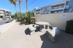A patio area with a round table and two benches, surrounded by a low wall and palm trees.
