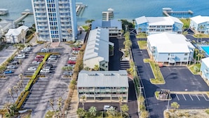 An aerial view of a coastal hotel with a parking lot, a large building with balconies, and a marina with docks.
