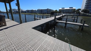A waterfront promenade with a patterned walkway, wooden docks, and modern buildings in the background.