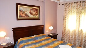 A neatly made bed with a striped bedspread, a framed painting above it, and a nightstand with a lamp.