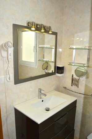 A bathroom with a large mirror, a sink, and a hairdryer on the wall. - Cozy Family Apartment. WiFi. Mountain views. Work Space  (Nerja)