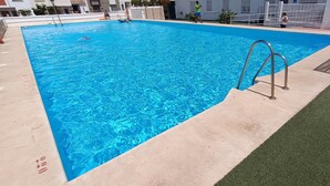 A rectangular swimming pool with clear blue water, a metal ladder, and a lifebuoy on the wall.
