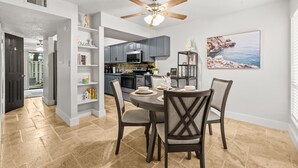 Une cuisine moderne avec des meubles gris, un coin repas doté d’une table ronde et de chaises, et un ventilateur de plafond.