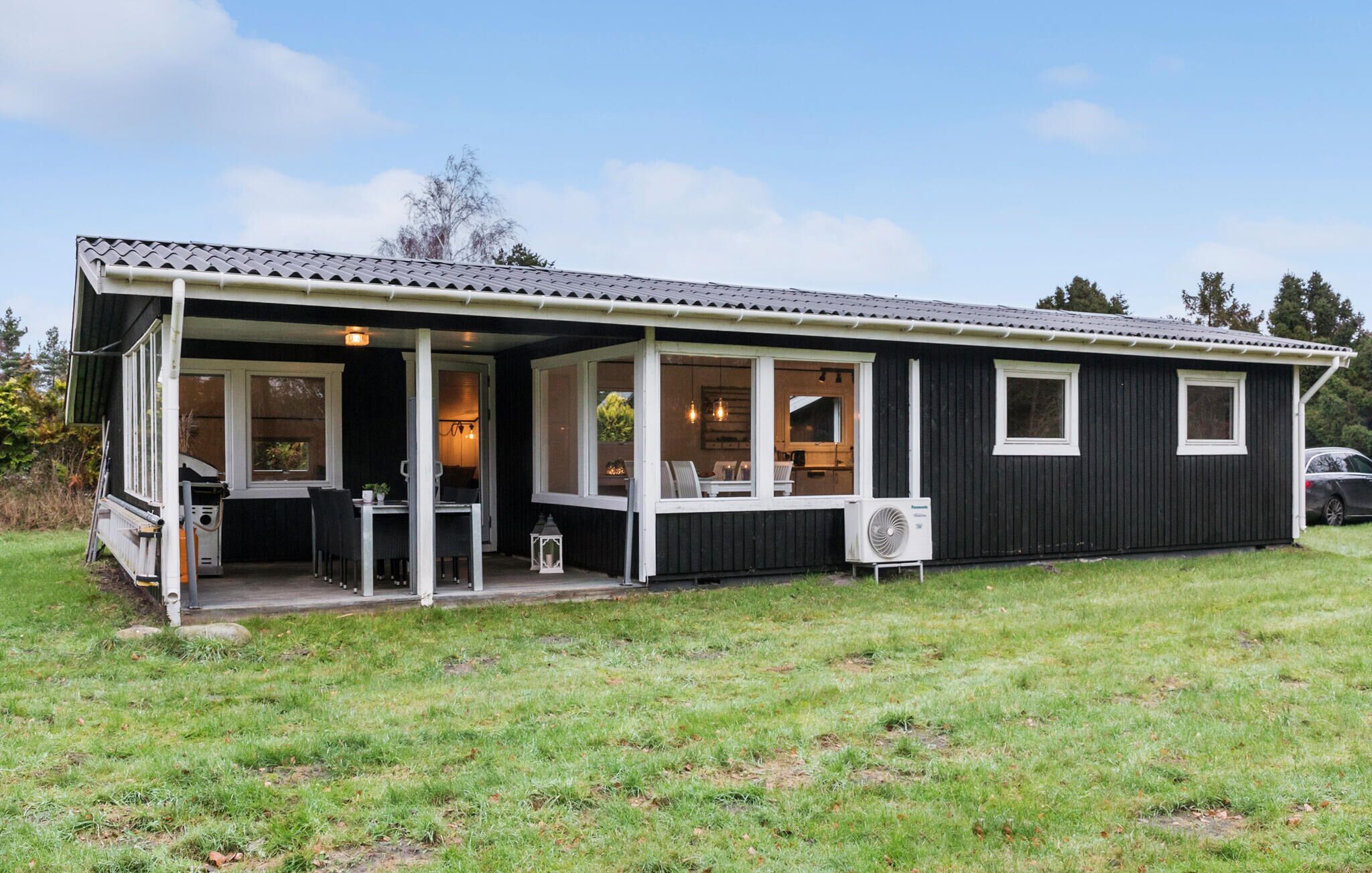 A single-story house with a covered porch, a dining area with chairs and a table, and a small kitchen area.