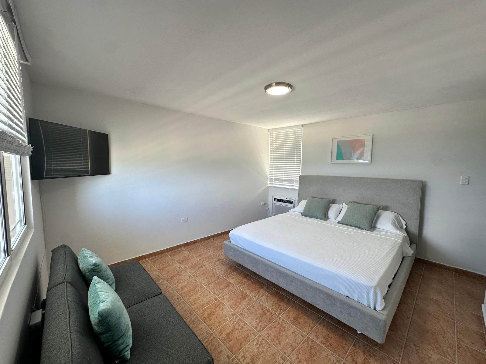 A bedroom with a bed, a sofa, a TV, and a window with blinds.