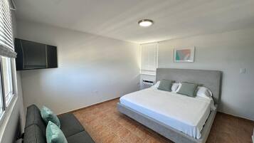 A bedroom with a bed, a sofa, a TV, and a window with blinds.