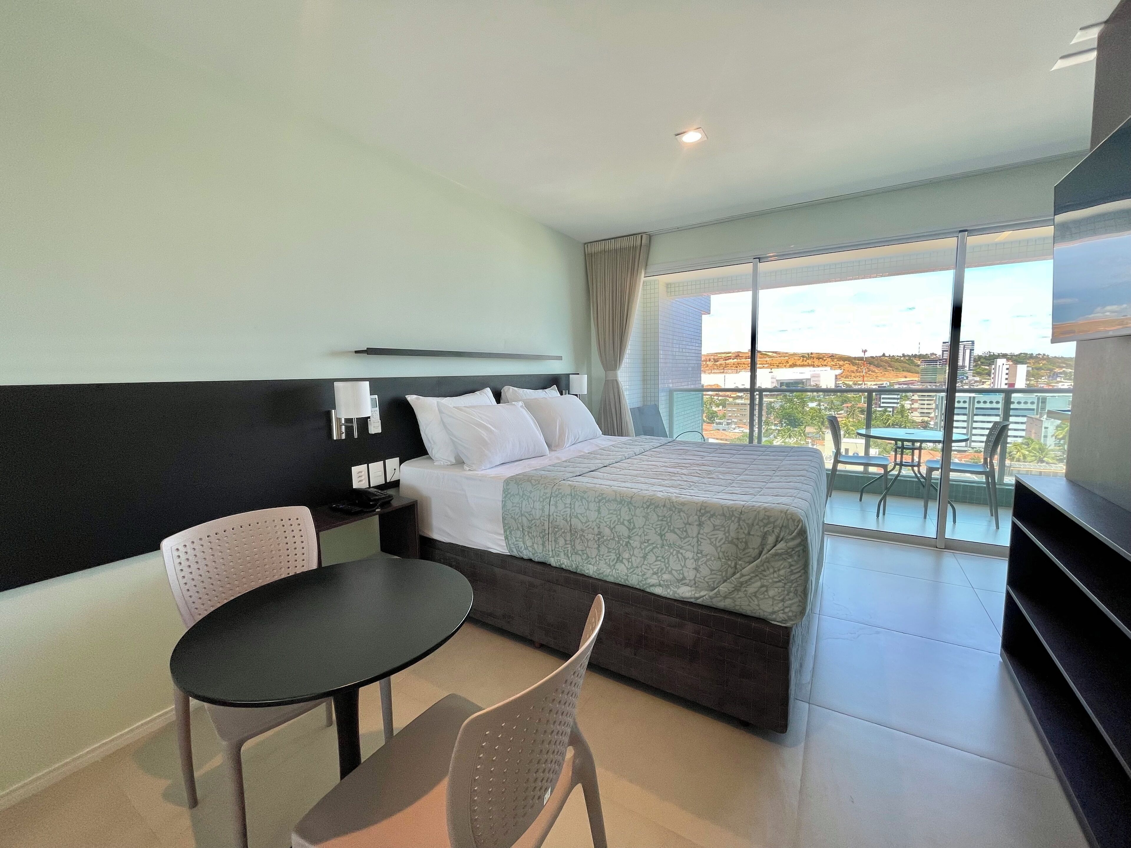 Habitación de hotel con cama, escritorio, silla y balcón con vistas.