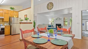 A dining area with a wooden table set for four, surrounded by wooden chairs. There is a kitchen area with wooden cabinets and a refrigerator to the left. - Spacious 4BR Near FSU & A&M | BBQ, Deck, Game Room (Tallahassee)