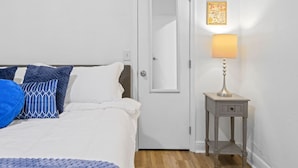 A bedroom with a bed, pillows, a nightstand with a lamp, a door, and two wall-mounted maps. - Spacious 4BR Near FSU & A&M | BBQ, Deck, Game Room (Tallahassee)