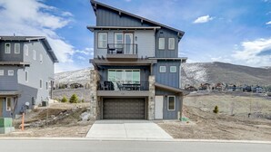 Une maison moderne à deux étages, dotée d’un garage, d’un balcon et offrant une vue sur un paysage vallonné.