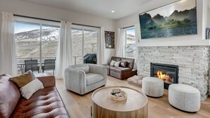 Un salon moderne avec une cheminée, de grandes fenêtres, un canapé, une table basse et un tableau représentant un paysage.