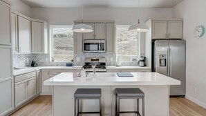 Une cuisine moderne dotée d’un îlot central, de luminaires suspendus et offrant une vue sur l’extérieur.
