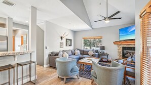 A spacious living area with a fireplace, a large TV, and a ceiling fan.